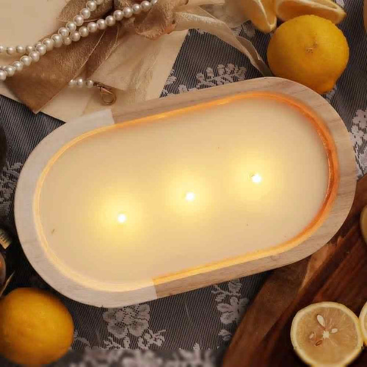 Oval wooden citronella candle with three wicks emitting warm glow and citrus aroma