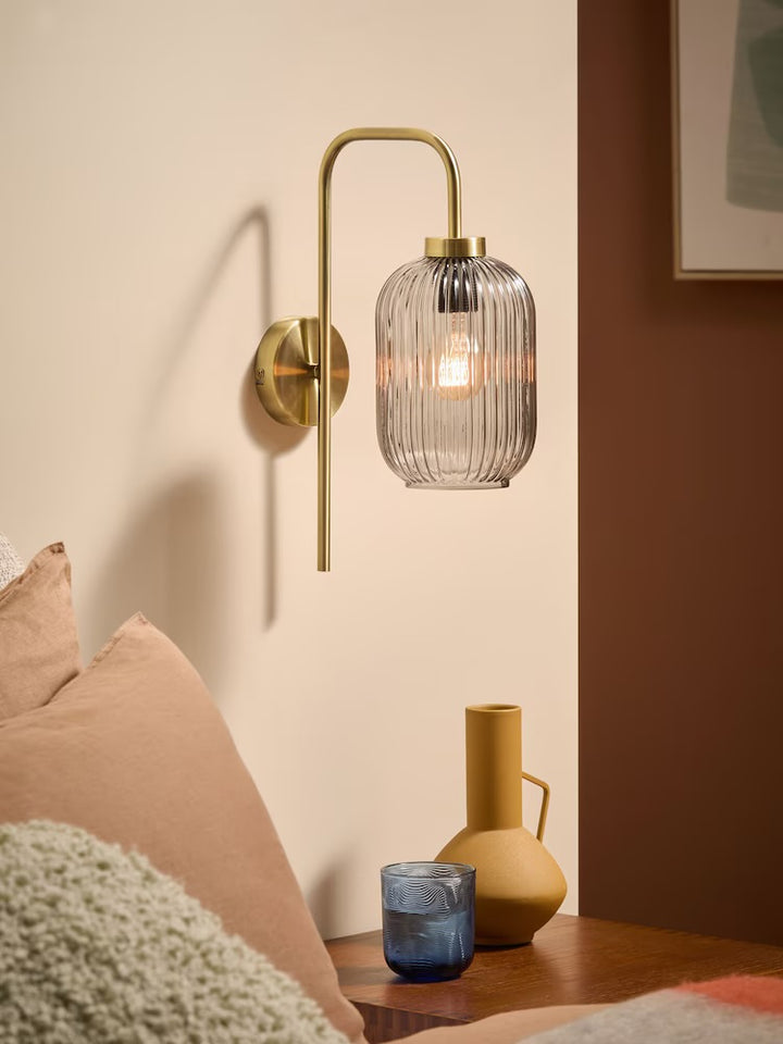 Modern wall sconce with ribbed glass shade and brass arm above a bedside table