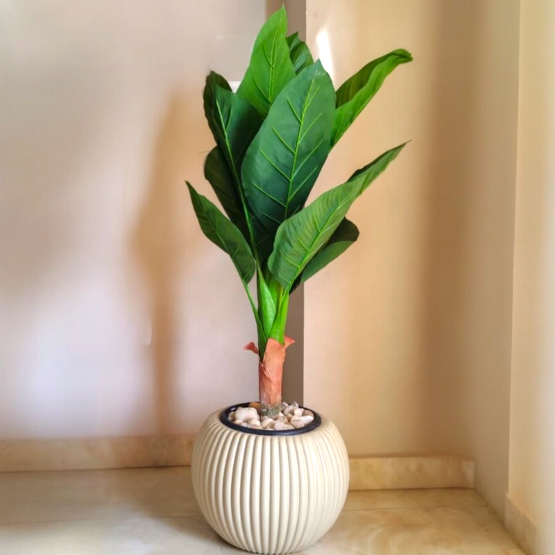 An artificial banana leaf plant with broad green leaves in a ribbed beige ceramic pot.