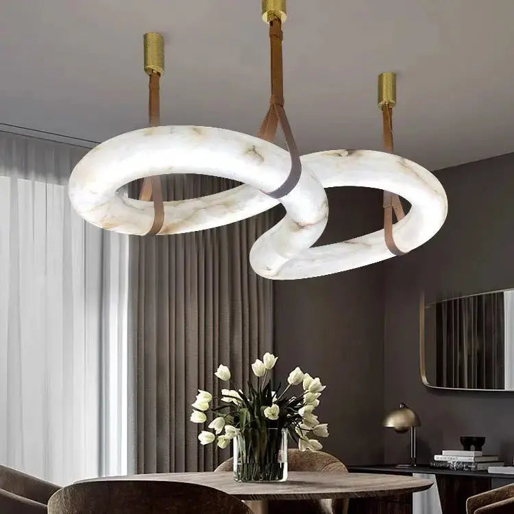 Modern three-loop white marble-effect LED chandelier with brass suspension hanging above a dining table in a contemporary living and dining room.