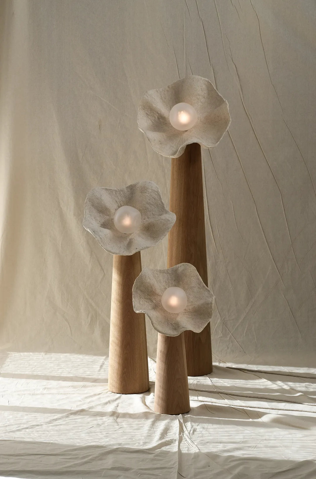 Organic floral sculptural floor lamp with three natural wood stems and textured flower-shaped shades emitting soft warm light.