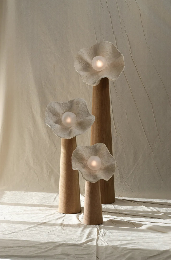 Organic floral sculptural floor lamp with three natural wood stems and textured flower-shaped shades emitting soft warm light.