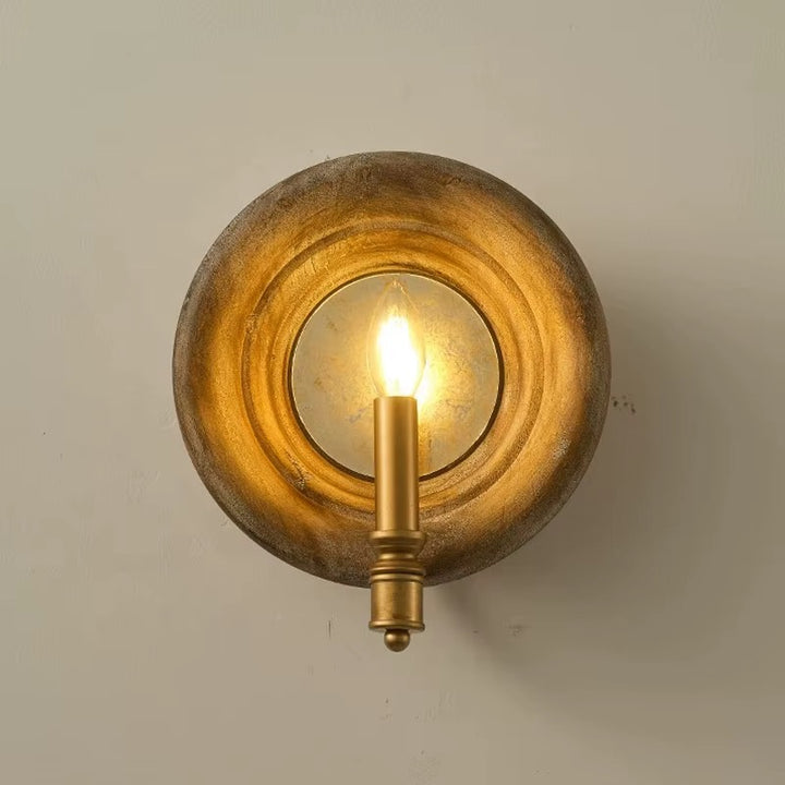 Vintage gold round wall sconce with a circular layered backplate and exposed glowing bulb