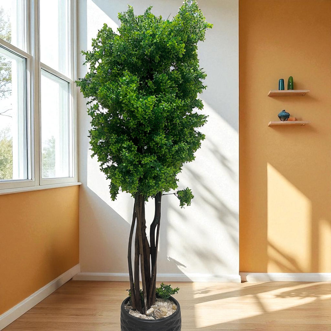 Tall artificial indoor tree with natural trunk and dense green foliage in a decorative pot.