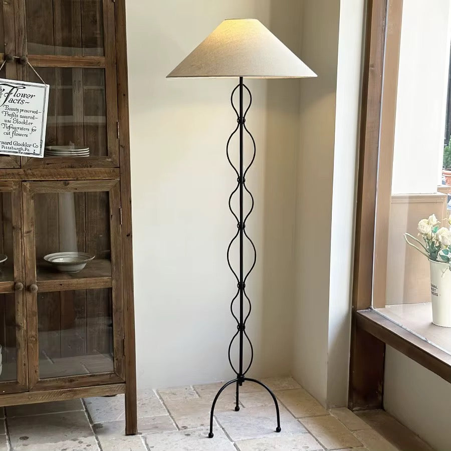 Black metal loop floor lamp with a beige fabric shade beside a rustic wooden cabinet