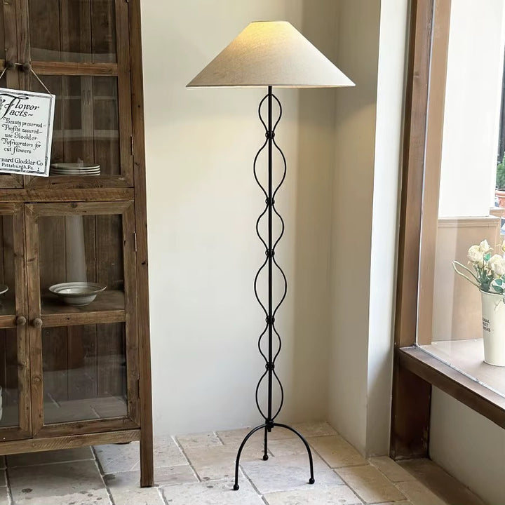 Black metal loop floor lamp with a beige fabric shade beside a rustic wooden cabinet