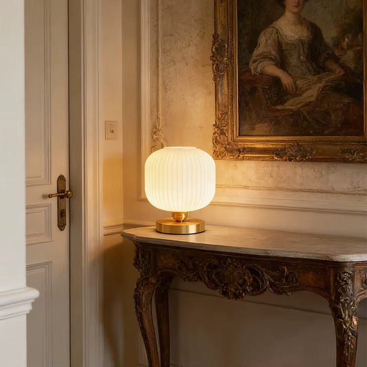 Ribbed opal glass table lamp with a brass base displayed on an ornate console table in an elegant hallway
