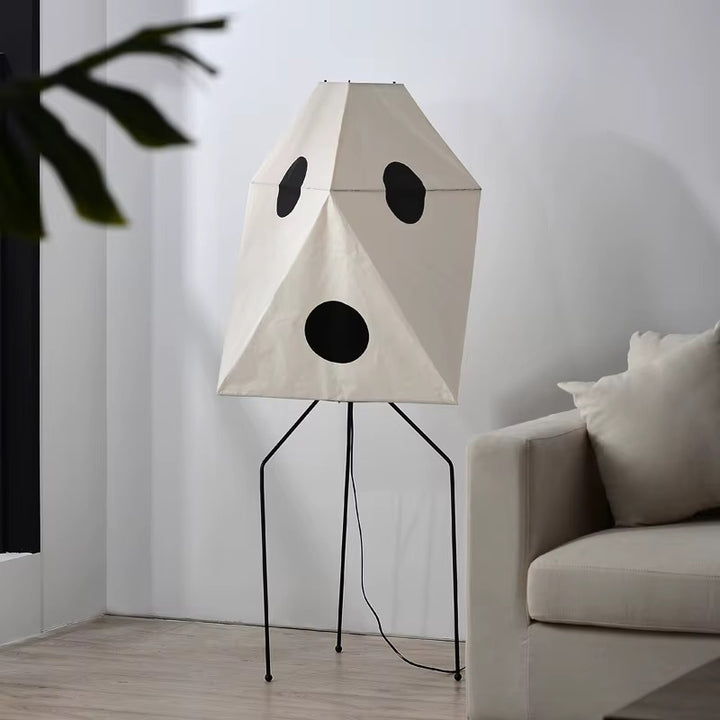 Geometric white dog-inspired floor lamp with a faceted shade, black metal legs, and a playful face design beside a sofa