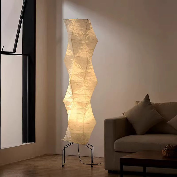 Tall sculptural warm-white paper floor lamp with an organically shaped shade and black metal frame beside a sofa