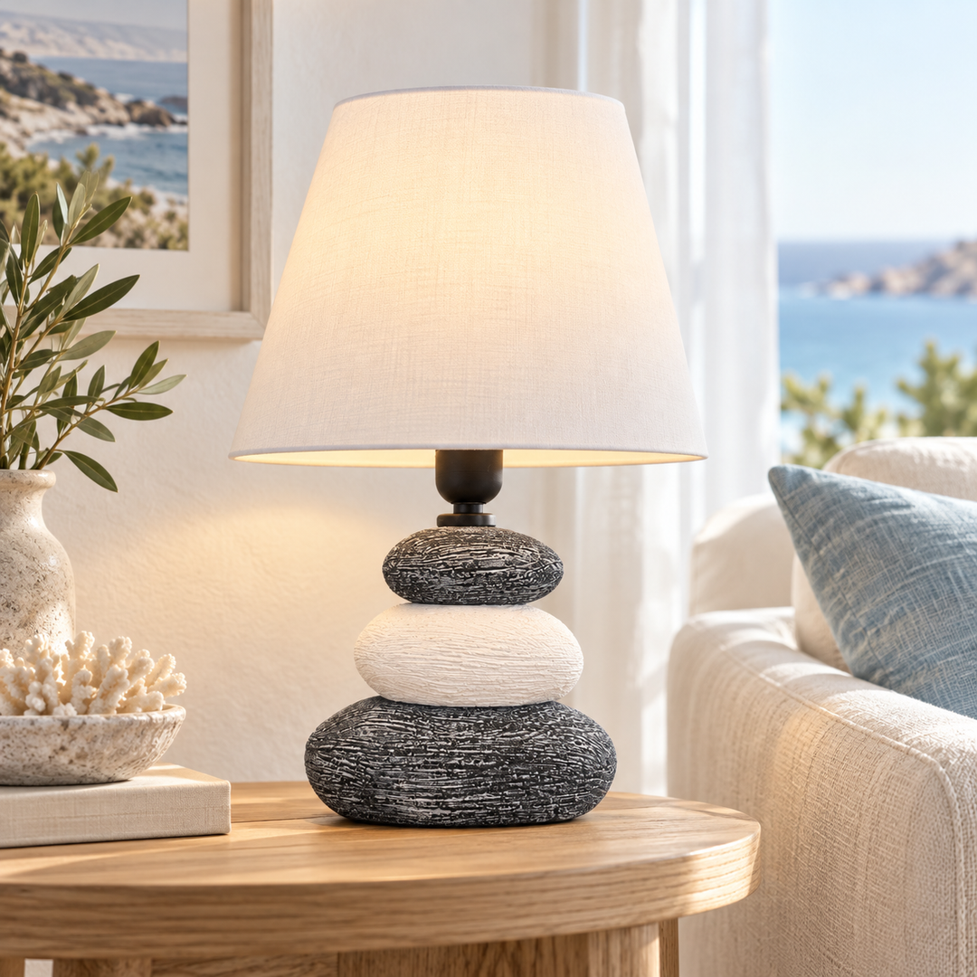 Table lamp with a stacked charcoal and cream textured base and an ivory fabric shade on a round wooden side table