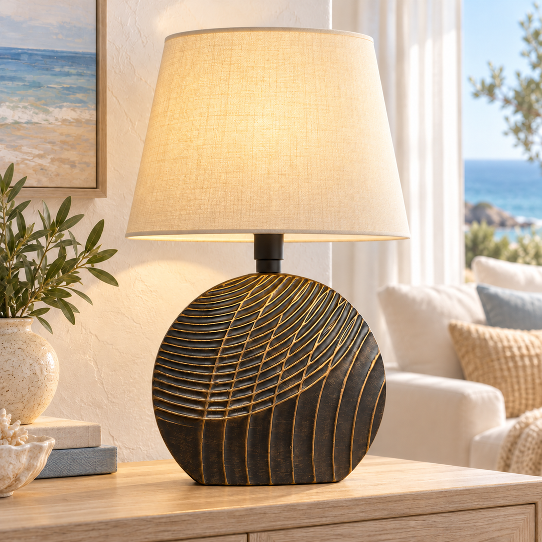 Sculptural black table lamp with raised gold-toned lines and a beige fabric shade on a wooden console