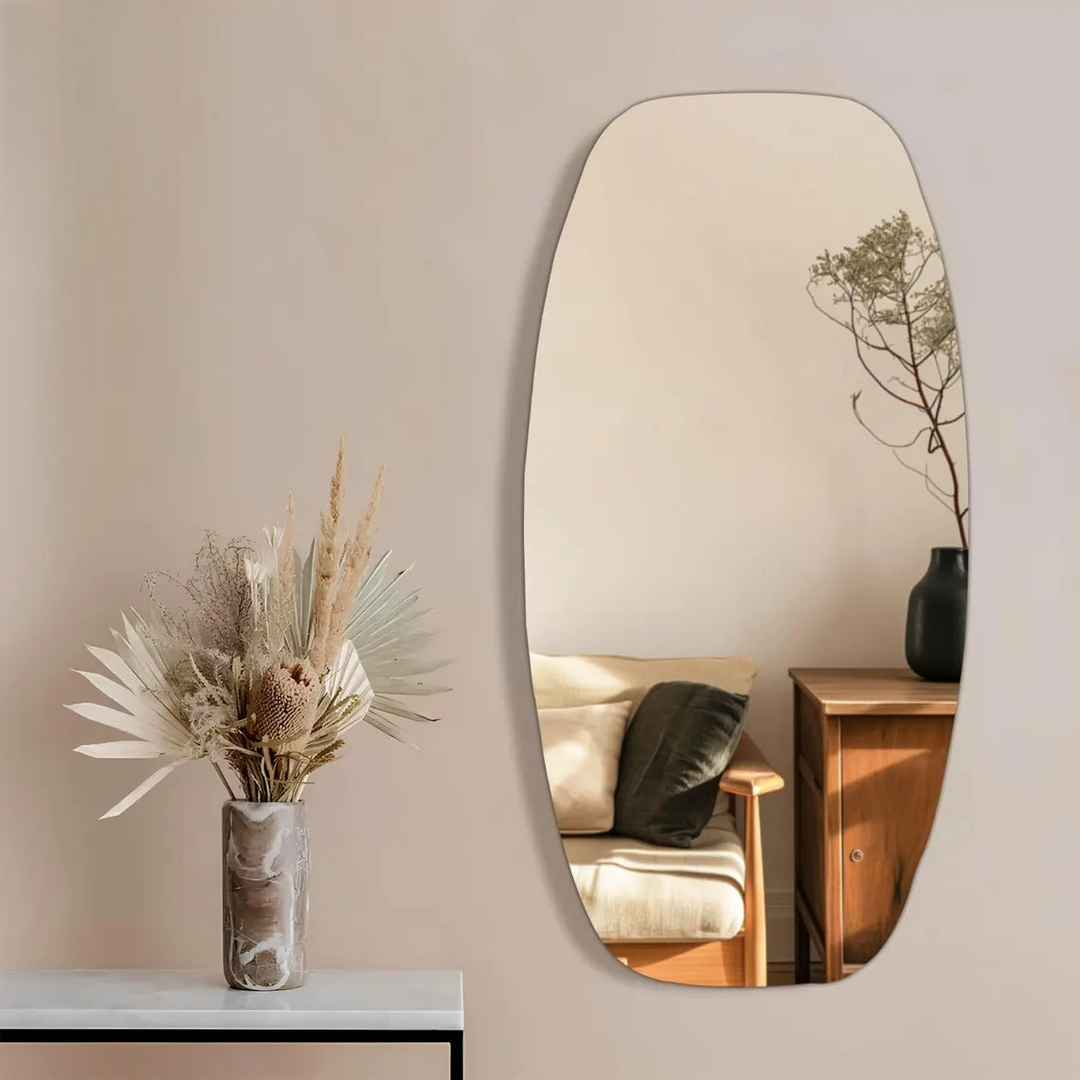 Large oval mirror on a wall with a vase of dried plants on a surface below.