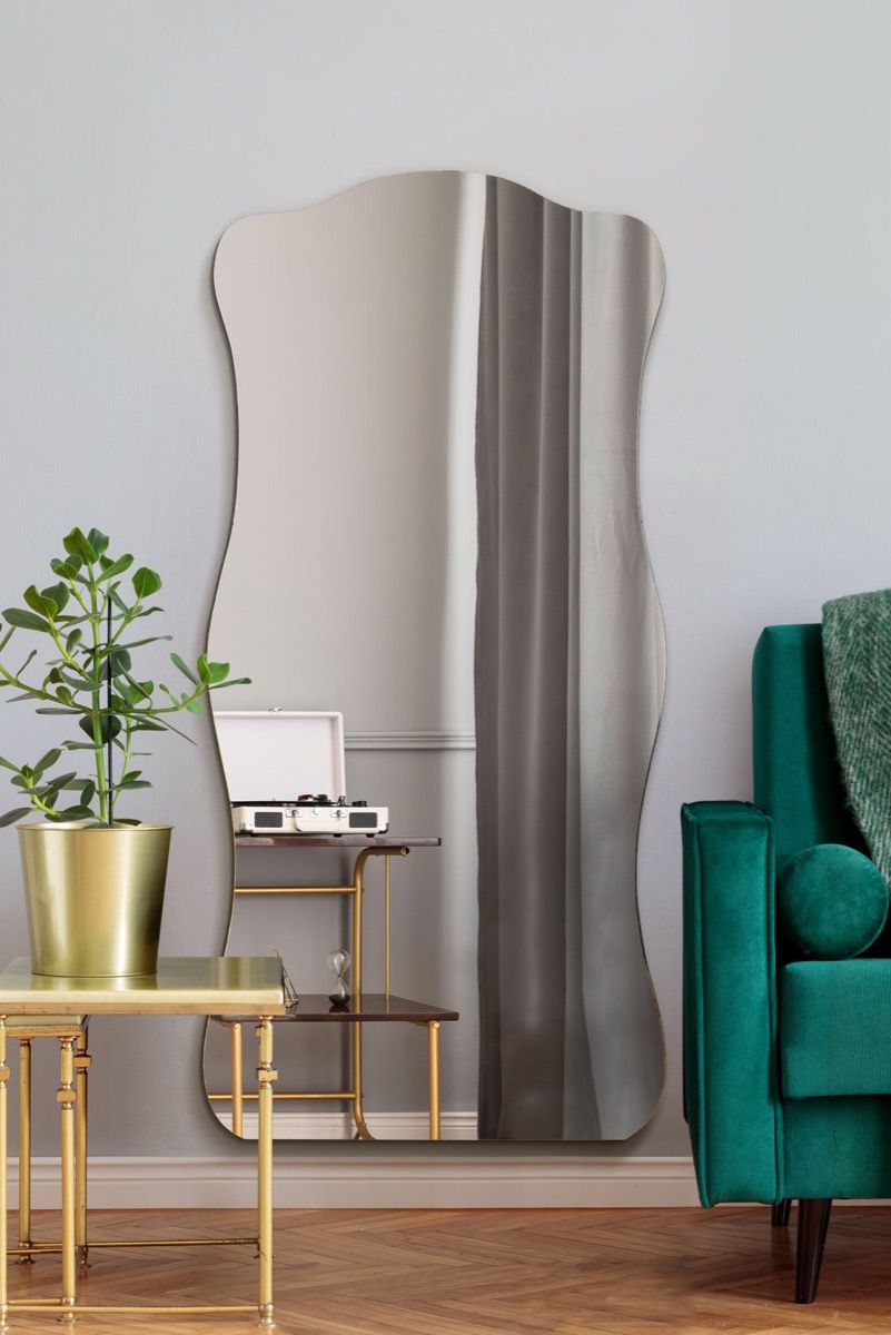 Modern interior with a large wavy mirror, green armchair, and gold side table.