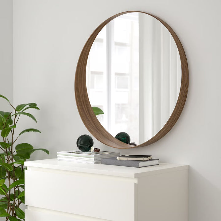 Round dark-wood wall mirror above white dresser in modern bedroom