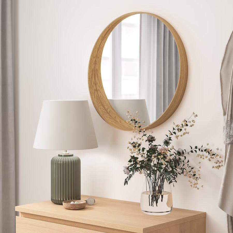 Round wooden wall mirror above dresser with lamp and vase
