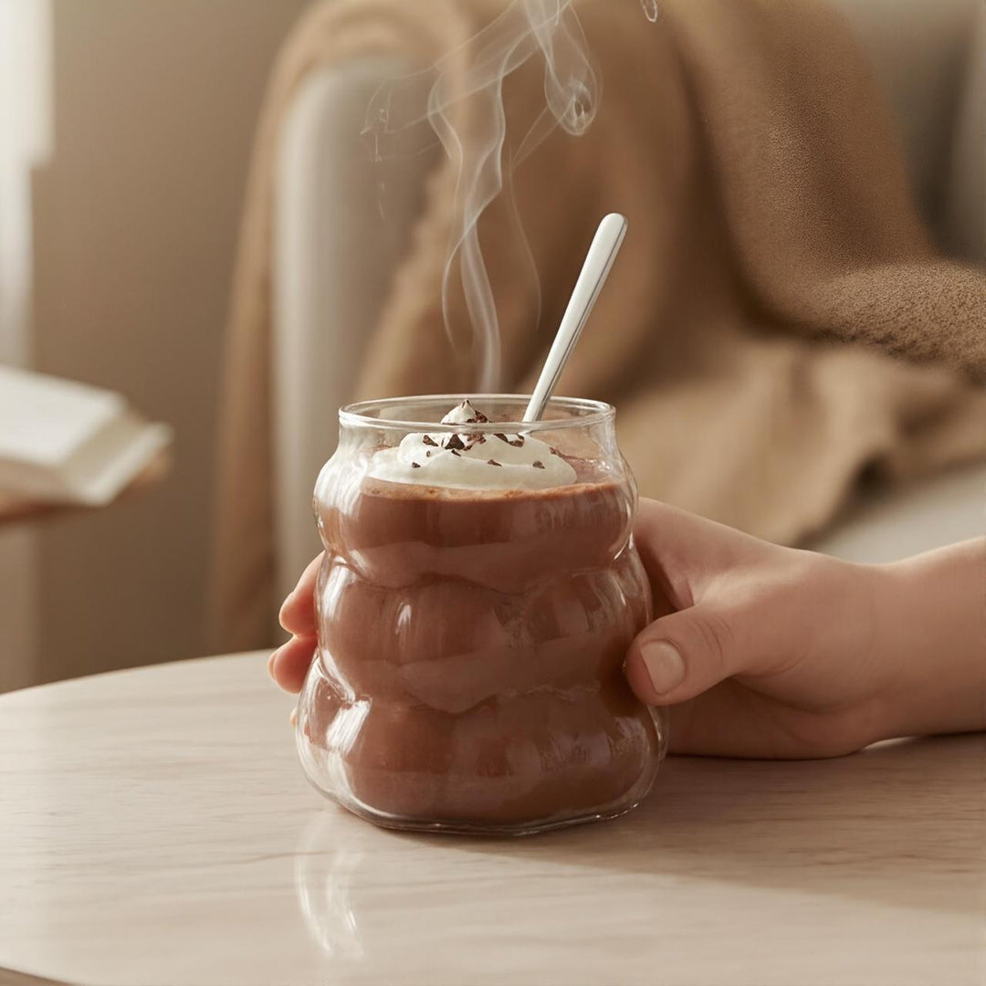 Hand holding a glass of hot chocolate with steam, cozy indoor setting