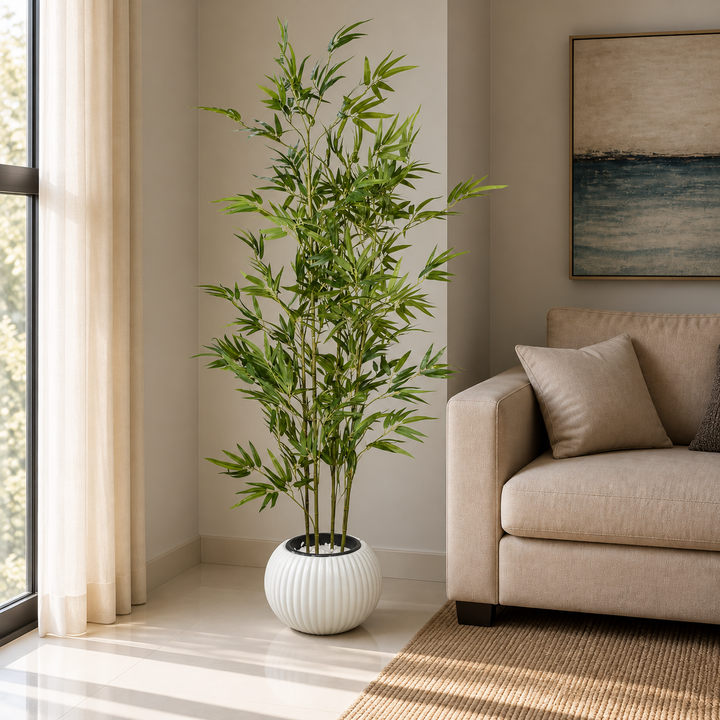 170 cm artificial bamboo tree with slender green canes and narrow leaves in a spherical white ribbed pot beside a beige sofa.