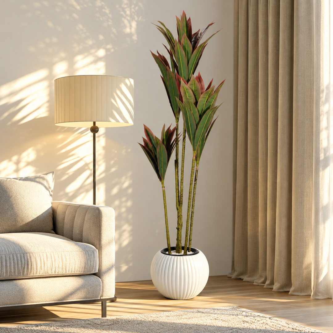 180 cm artificial dracaena with green and burgundy pointed leaves on staggered canes in a spherical white ribbed pot beside a cream armchair.