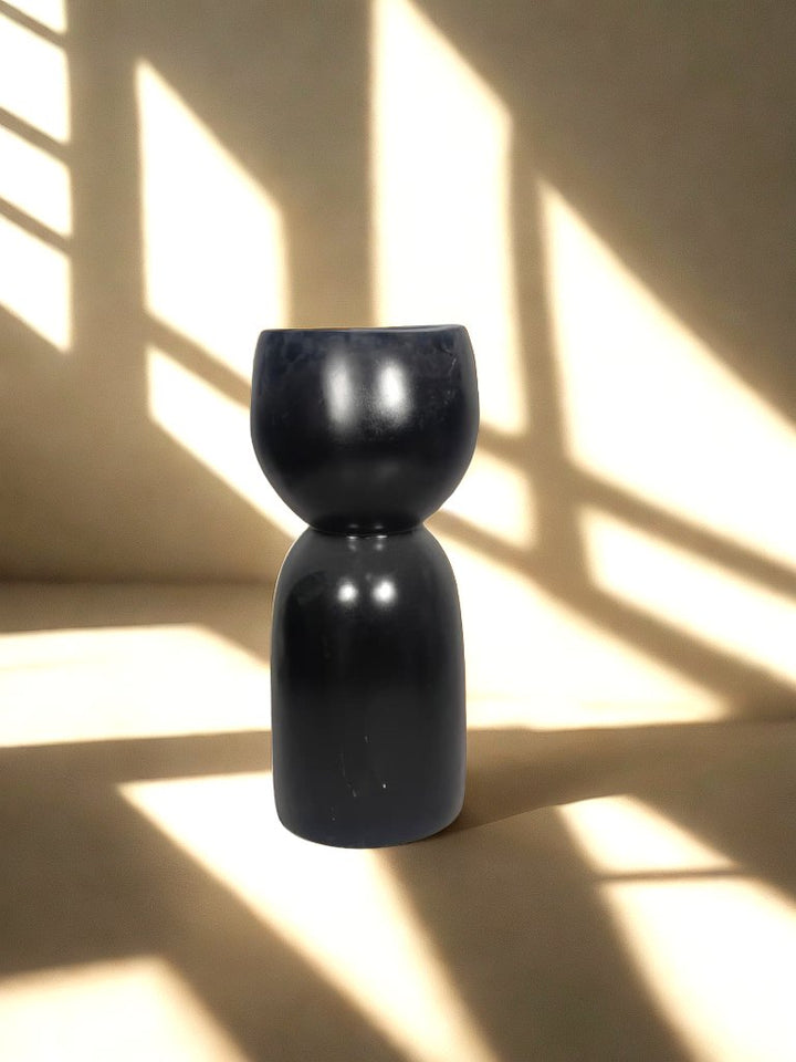 Glossy black fiberglass planter with a rounded bowl and tall sculptural pedestal-style base in a softly lit neutral interior.