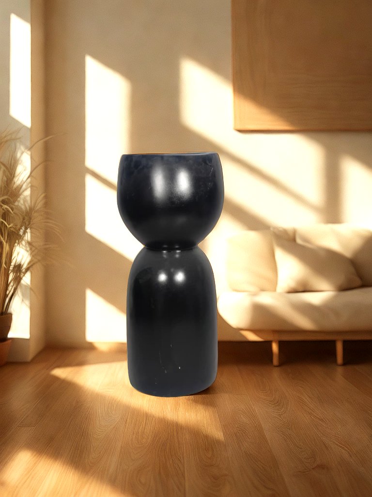Glossy black fiberglass planter with a rounded bowl and tall sculptural pedestal-style base styled in a warm living room.