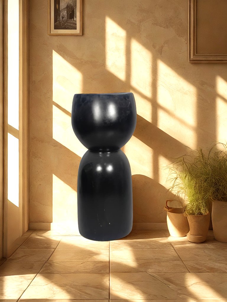 Glossy black fiberglass planter with a rounded bowl and tall sculptural pedestal-style base displayed in a neutral entryway.