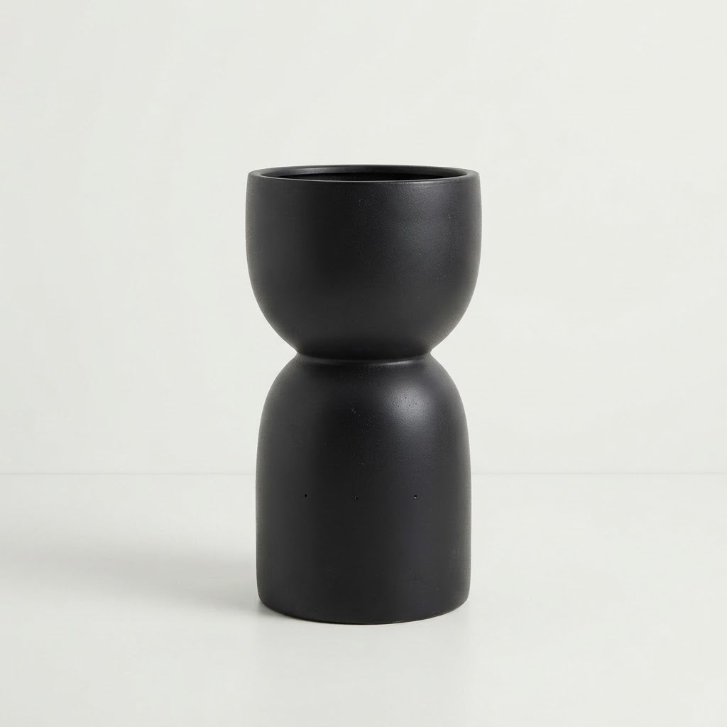 Glossy black fiberglass planter with a rounded bowl and tall sculptural pedestal-style base on a plain white studio background.