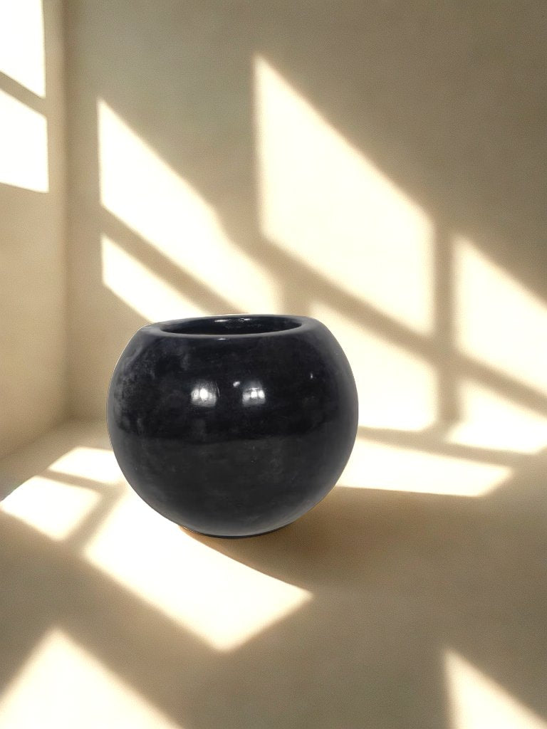 Glossy black round fiberglass planter with a wide circular opening in a softly lit neutral interior.
