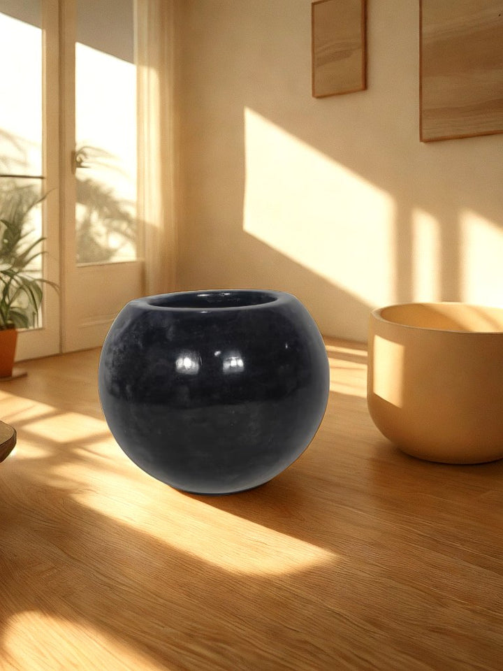Glossy black round fiberglass planter with a wide circular opening styled in a warm living room.