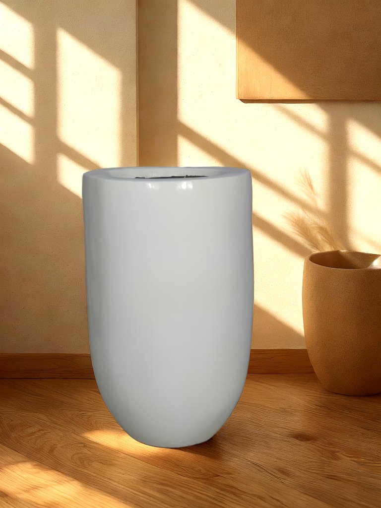Tall glossy white fiberglass planter with a rounded base styled in a warm living room.
