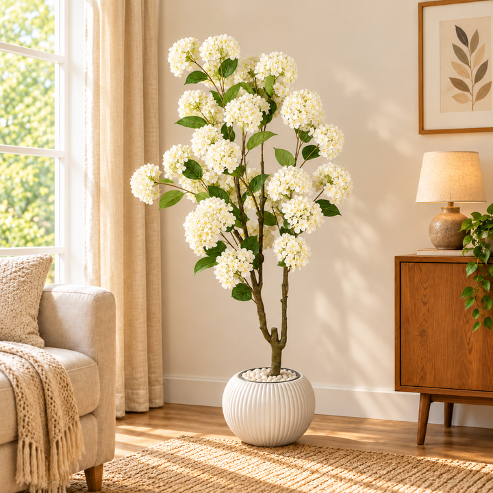 165 cm artificial white hydrangea tree with green leaves in a spherical white ribbed pot styled with white decorative pebbles.