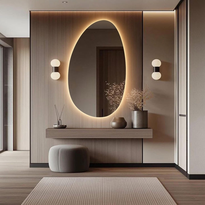 A large oval-shaped backlit makeup mirror with LED lights, mounted on a wall above a wooden console table in a modern bathroom setting.