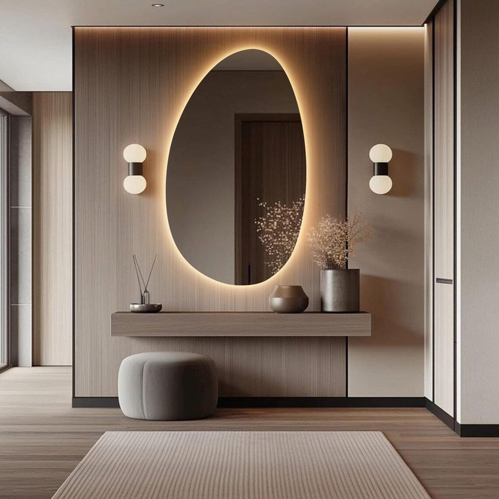 A large oval-shaped backlit makeup mirror with LED lights, mounted on a wall above a wooden console table in a modern bathroom setting.