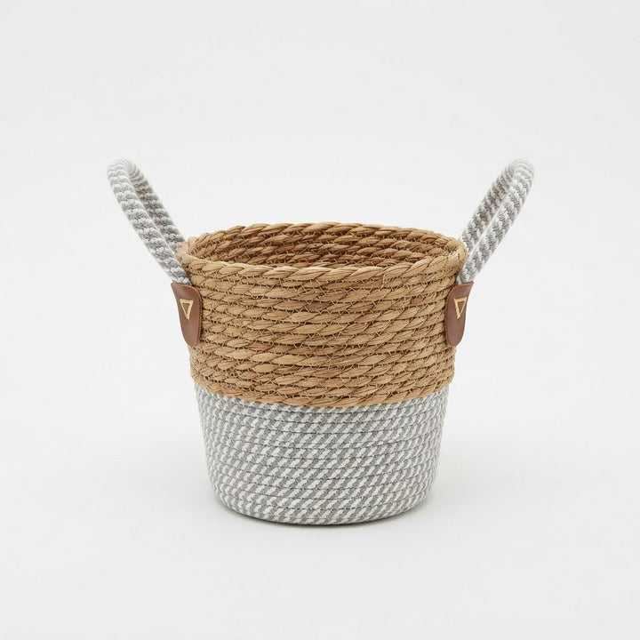 Natural woven basket planter with grey and white rope base and two loop handles on a plain white studio background.