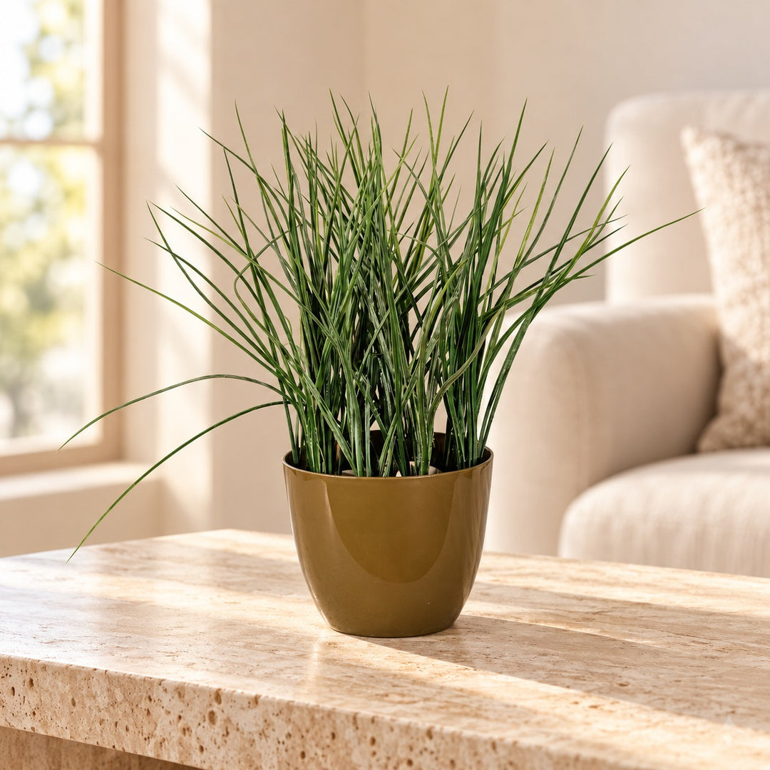 Fine-bladed artificial green grass in a smooth olive-gold tapered pot styled on a travertine table in an elegant neutral living room