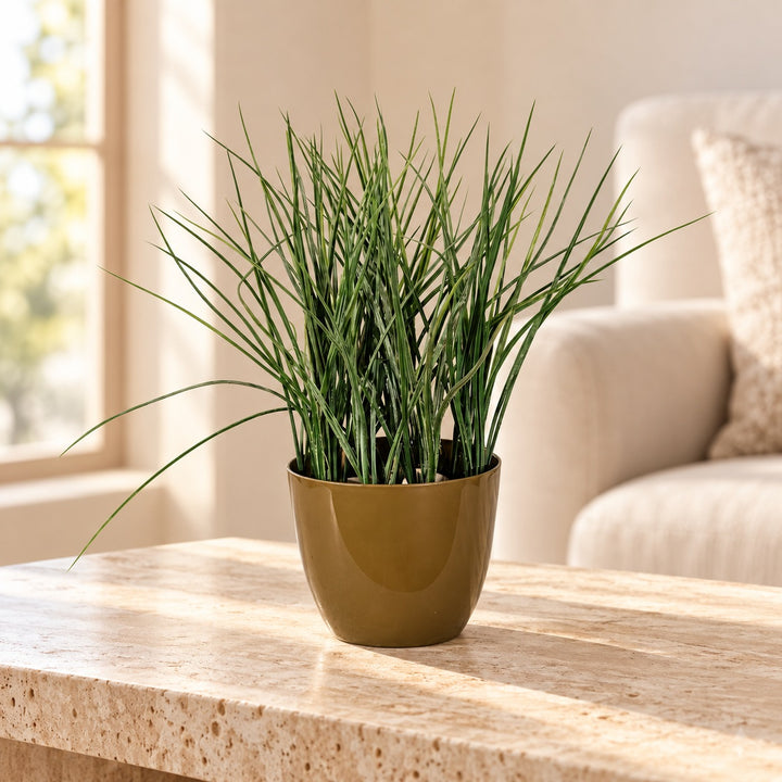Fine-bladed artificial green grass in a smooth olive-gold tapered pot styled on a travertine table in an elegant neutral living room