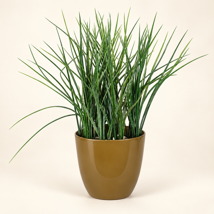Fine-bladed artificial green grass in a smooth olive-gold tapered pot on an ivory studio background