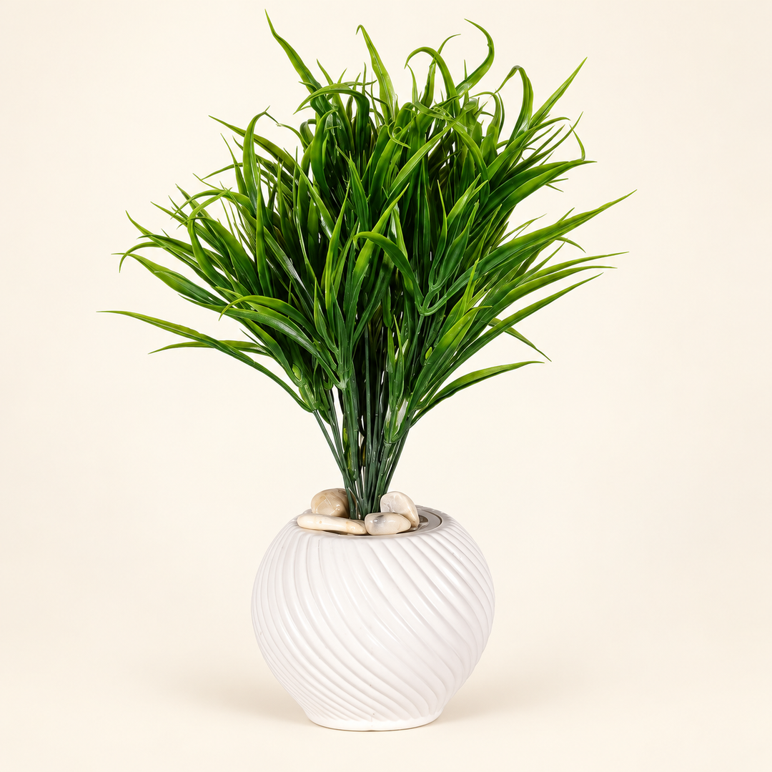 Artificial green grass with curling blades in a round white spiral-ribbed pot topped with pale stones on an ivory studio background