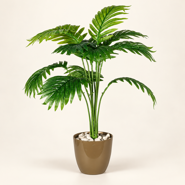 Artificial palm with arching green fronds in an olive-gold pot topped with pale decorative stones on an ivory studio background