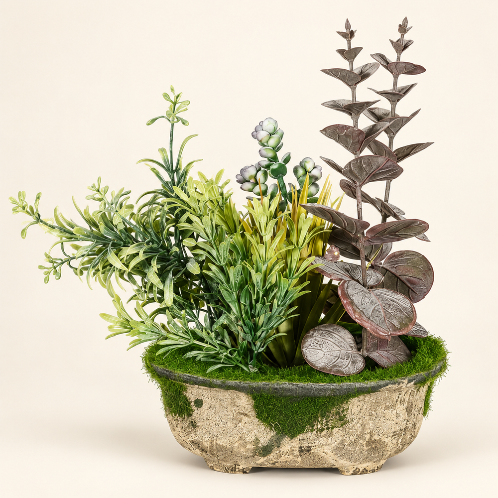 Artificial arrangement with muted eucalyptus-style leaves, green meadow foliage and moss in a rustic oval planter on an ivory studio background