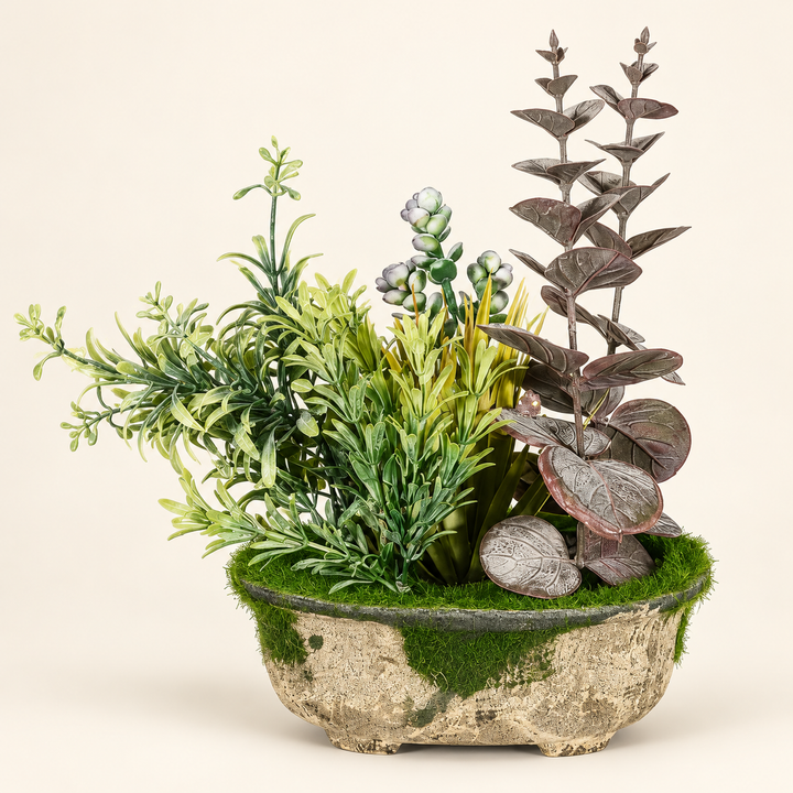 Artificial arrangement with muted eucalyptus-style leaves, green meadow foliage and moss in a rustic oval planter on an ivory studio background