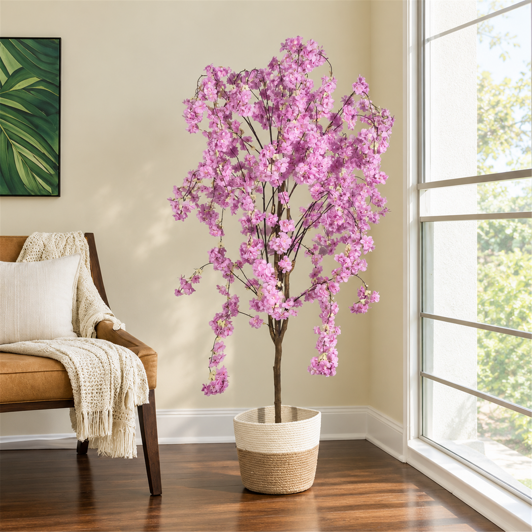 155 cm pink flowering artificial tree with cascading blossoms and its cream and beige woven planter beside a sunlit window.