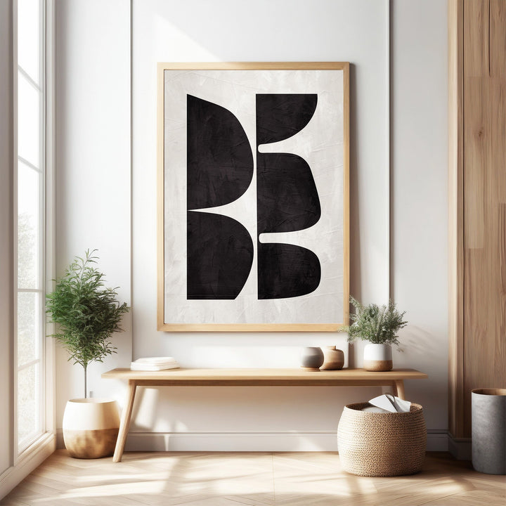 Wadi Home abstract geometric wall art with black organic shapes on textured off-white background, framed in light wood.