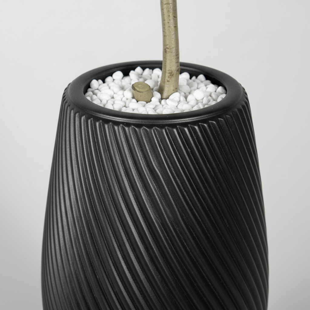 Wadi Home artificial aralia tree in a modern black textured spiral planter with decorative white stones at the base.
