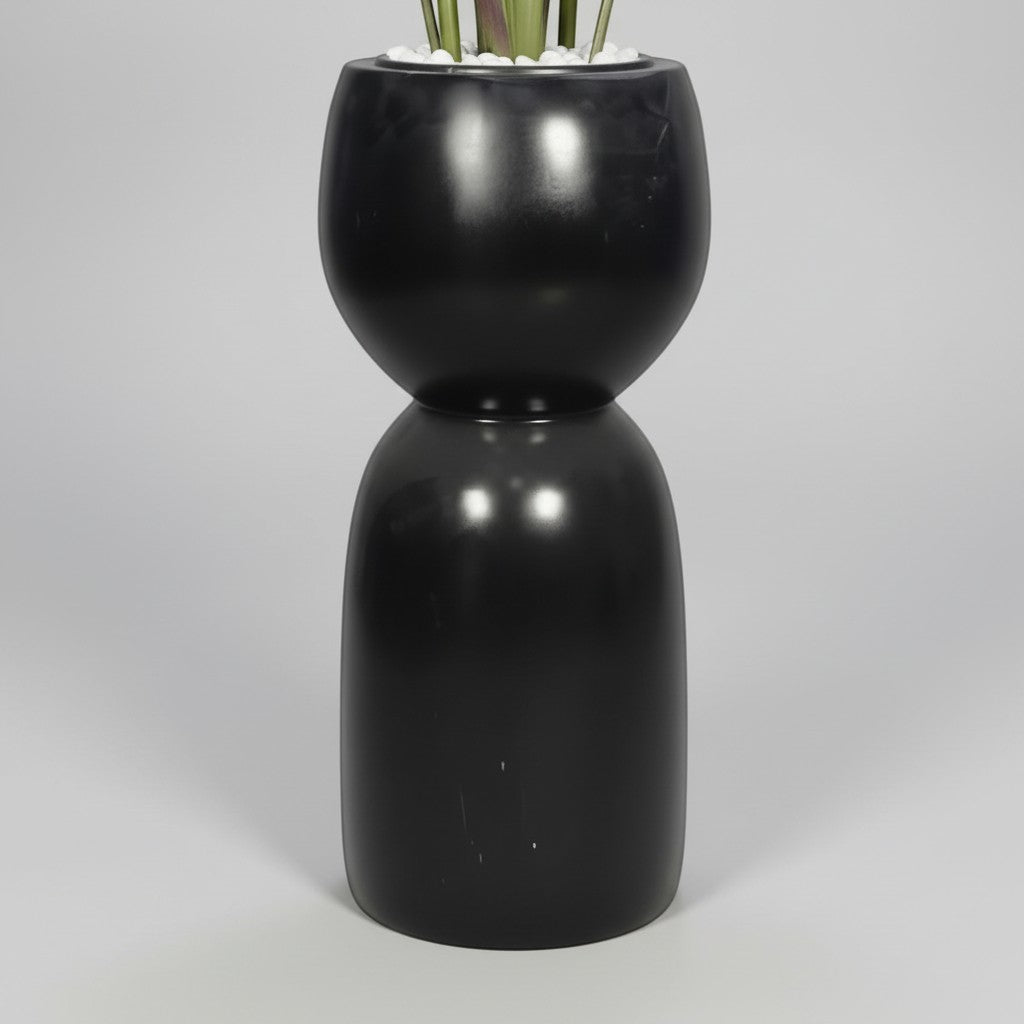 Wadi Home artificial Bird of Paradise plant in a modern sculptural black hourglass floor planter with white stones.