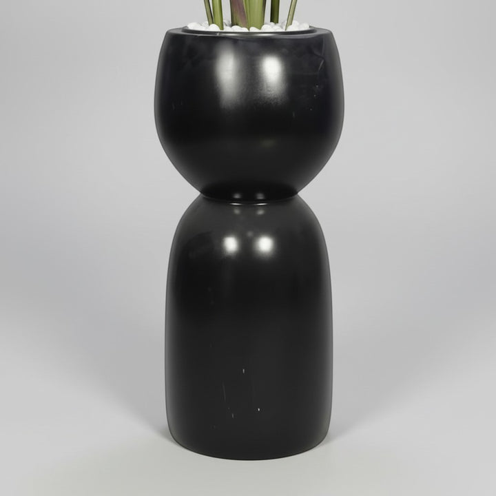 Wadi Home artificial Bird of Paradise plant in a modern sculptural black hourglass floor planter with white stones.