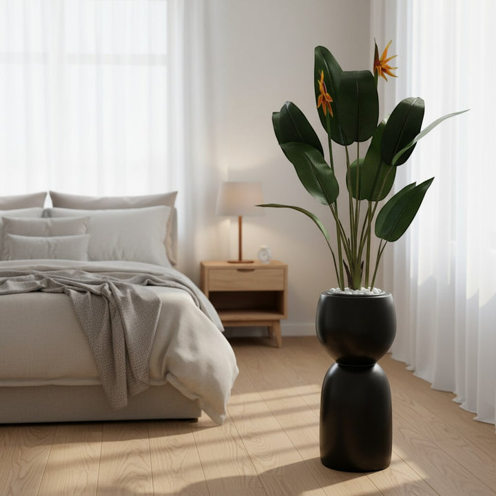 Wadi Home artificial Bird of Paradise plant with orange blooms in a sculptural black floor planter in a bedroom.