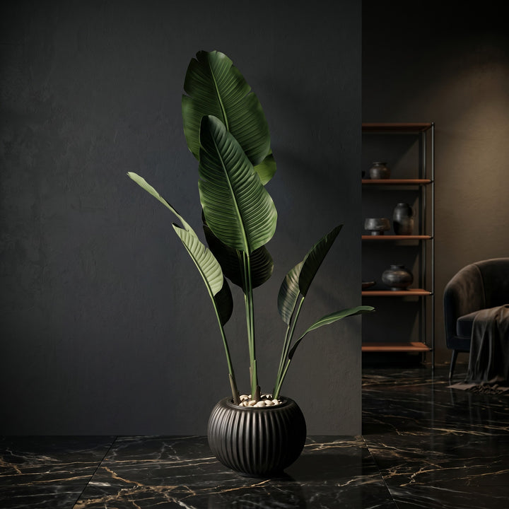 Wadi Home large artificial Bird of Paradise plant in a ribbed black planter with white stones on a marble floor.