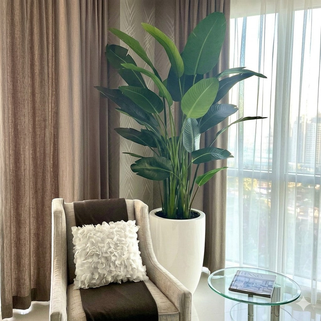 Wadi Home artificial Bird of Paradise plant with large green leaves in a tall white pot next to a modern armchair.