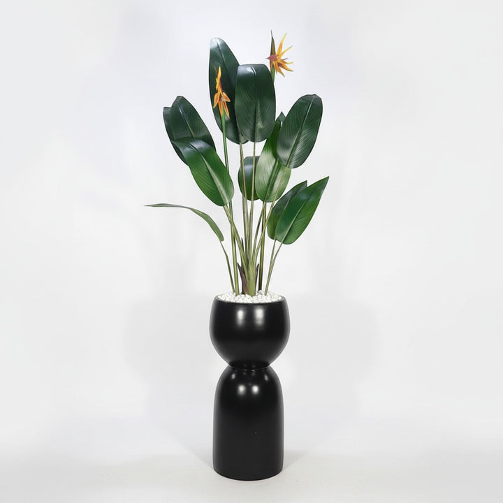 Wadi Home artificial Bird of Paradise plant with green leaves and orange flowers in a modern black hourglass planter.
