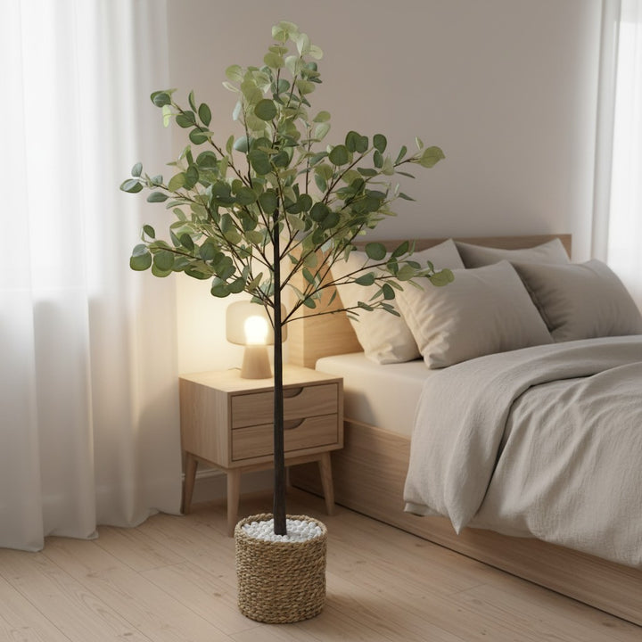 Wadi Home artificial eucalyptus tree in a woven basket with white stones, placed in a modern minimalist bedroom.